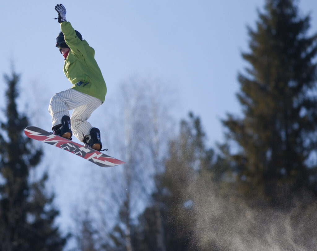 Snowboarder in the air wearing white pants and a green jacket