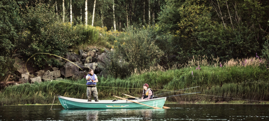 Two people fishing for salmon from a boat in the Klarälven river in the summer.