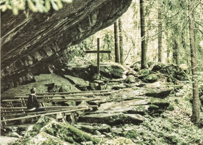 Ett kors och några bänkar under ett stort klippblock